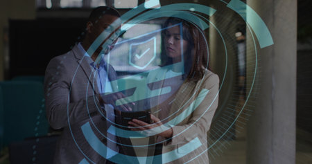 Two colleagues wearing suits reviewing tablet in office corridor, with holographic security overlay. Corporate, technology, modern, collaboration, digital, futuristic, professionalの写真素材