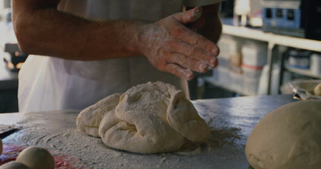 Pressing flour-covered hands kneading dough on steel worktable in bakery, with ingredient canisters. Bakery, craftsmanship, rustic, artisanal, culinary, texture, kneadingの写真素材
