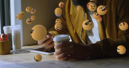 Holding smartphone, man wearing brown jacket using tablet, sipping coffee at cafe, floating emojis....