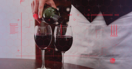 Server wearing white apron pouring red wine into two glasses at bar table, with green bottle....