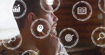 Contemplating man resting hand on chin at office desk, with floating digital interface icons....