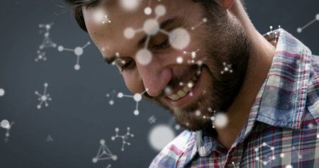 Smiling man in plaid shirt, looking downward in grey studio, with molecular graphics, copy space. Scientist, innovation, technology, communication, modern, professional, researchの写真素材