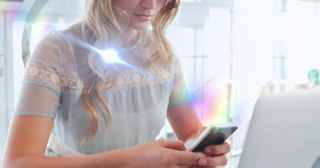 Using smartphone and typing on laptop, woman at office desk in daylight, pastel lace blouse. Professional, modern, minimalist, technology, female, workspace, brightの写真素材