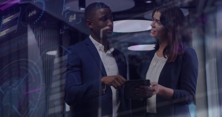 Collaborating professionals in suits analyzing data on tablet behind glass wall with digital charts....