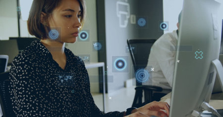 Typing female office worker in patterned top analyzing at office, with monitors keyboards overlays....