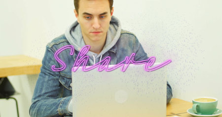 Typing man wearing denim jacket at cafe, with laptop showing neon-pink Share text and green mug....
