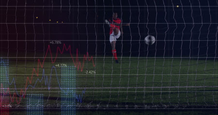 Soccer player kicking ball in red uniform on grass field at night, with net, data overlays. Athlete,...