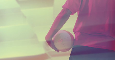 Standing woman in red jersey black shorts holding volleyball at gym under pink lighting, copy space. Athletic, sport, fitness, dynamic, competition, activewear, vibrantの写真素材