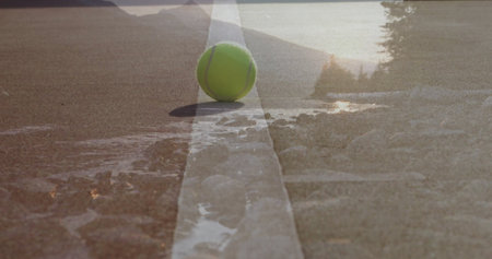 Resting tennis ball sitting on white painted line on outdoor court, with puddles and stones. Athletic, sports, vibrant, outdoor, nature, competition, textureの写真素材