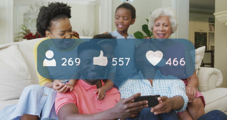 Scrolling extended family sharing smartphone posts in living room, with social media overlay icons. Family, multigenerational, leisure, interior, connection, happiness, modernの写真素材