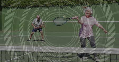 Swinging senior woman in pink tee hitting forehand on hardcourt, with rackets net hedge, copy space. Athletic, competition, greenery, active, outdoor, vitality, leisureの写真素材