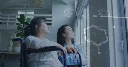 Supporting patient nurse in scrubs holding wheelchair at large window in lounge, with stethoscope....