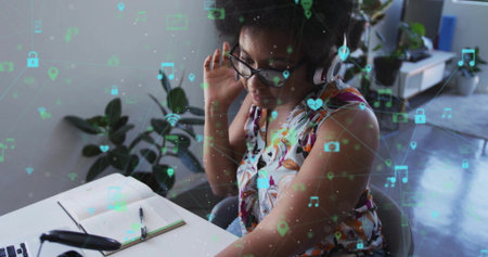 Woman typing on laptop adjusting headphones in home office with floating digital icons, copy space....
