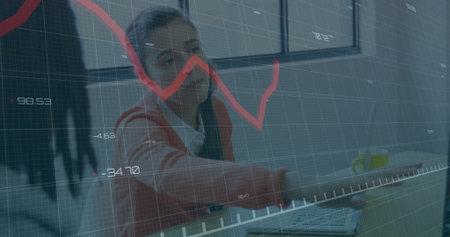 Typing office worker wearing orange cardigan using laptop at desk with red line graph overlay....
