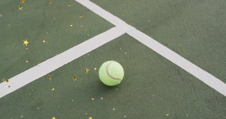 Resting tennis ball on outdoor tennis court near white lines, with gold star confetti, copy space....