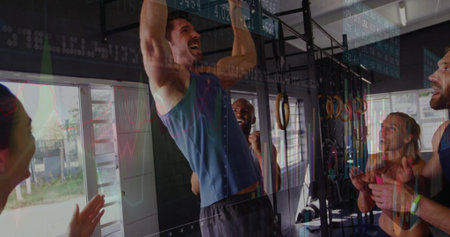 Muscular man in blue sleeveless shirt performing pull-up on bar in gym, with cheering partners....