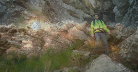 Hiker navigating gorge wearing green jacket harness belt backpack boots jagged rocks, copy space....