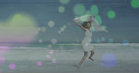 Woman in white dress running along beach holding white scarf, with ocean waves and bokeh overlays....