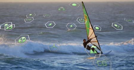 Cutting windsurfer in black wetsuit skimming sailboard on swells near sunset, copy space. Adventure,...
