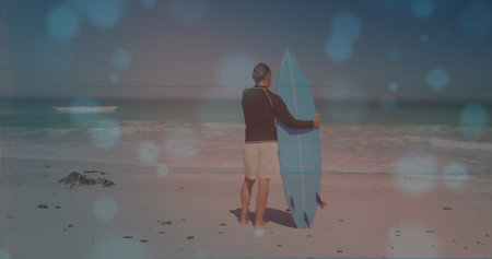 Mature man wearing black rash guard standing on sandy beach with blue surfboard and pebbles. Beach,...