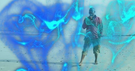Talking senior man holding smartphone at sandy shore, with cyan digital particles, copy space....