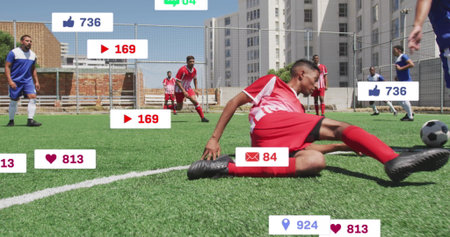 Sliding man in red uniform tackling opponent near soccer ball on pitch, with social media icons....