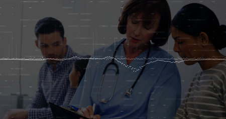 Writing white female doctor in blue scrubs on clipboard in medical exam room, with stethoscope....