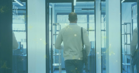 Walking man wearing light sweater in office corridor with glass partitions, carrying messenger bag....
