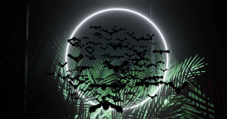 Flying silhouetted bats crossing dark stage space, with neon circle and illuminated palm leaves....