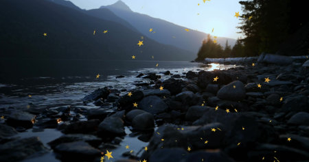 Bathing shoreline showing stones, water, driftwood, treed peaks and golden sparks at sunrise....