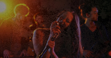 Singing female vocalist holding microphone near mouth on stage, with keyboard and electric guitar....