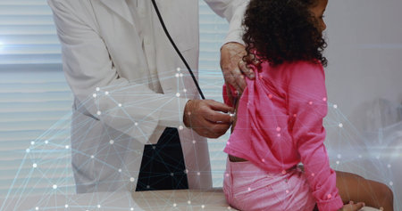 Examining senior doctor using stethoscope on seated child at exam table, digital network overlay. Healthcare, pediatrics, telemedicine, technology, diagnostics, clinic, innovationの写真素材