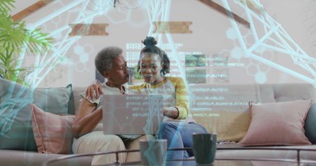 Sharing laptop screen mother and daughter sitting on sofa, with coffee table and mug. Intergenerational, bonding, family, relaxation, home, warm, contemporaryの写真素材