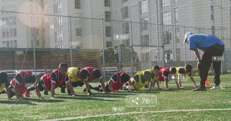 Youth soccer players wearing bibs performing push-ups on turf, with coach guiding and orange cones....