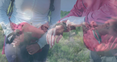 Hikers checking smartwatch in meadow, with trekking poles, backpack straps and jacket tied at waist. Adventure, exploration, wilderness, nature, outdoor activity, fitness, tranquilityの写真素材