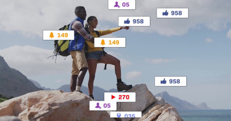 Pointing couple standing atop cliff overlooking ocean, with hiking backpacks, social media icons....