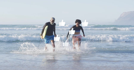 Running senior man and woman carrying yellow surfboard from surf at shoreline, wearing rash guards....
