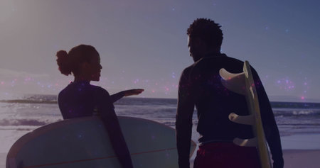 Watching surfers wearing wetsuits and shorts carrying longboard and surfboard at sunset on beach....