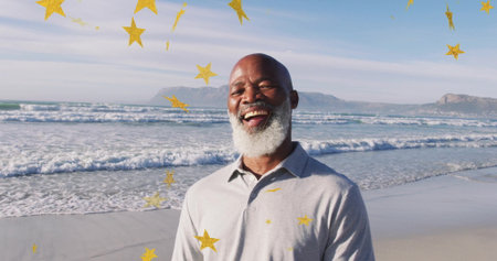 Smiling African American man in light grey shirt on beach, waves rolling. Senior, beach,...