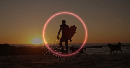 Standing male surfer holding surfboard on sandy beach at sunset, with neon ring and dogs. Beach,...