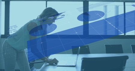 Leaning businesswoman examining laptop under chart overlays at conference table, copy space....