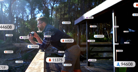 Leaning mature man pressing DSLR camera to eye on cabin deck, wearing plaid shirt and sunglasses....