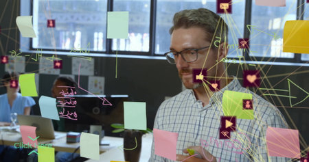 Checkered-shirted man writing on glass partition in office, with sticky notes and icons, copy space....