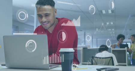 Leaning man wearing red sweater working on laptop at open-plan office with data visualizations....