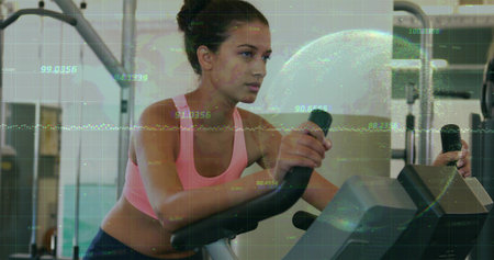 Woman in pink sports bra, leggings pedaling stationary bike in gym, with data overlay, weight racks....