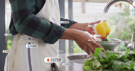 Woman wearing apron rinsing bell pepper under chrome faucet at kitchen sink, notification icons....