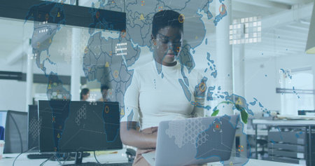 Working data analyst typing on silver laptop in open-plan office, with digital world map overlay....