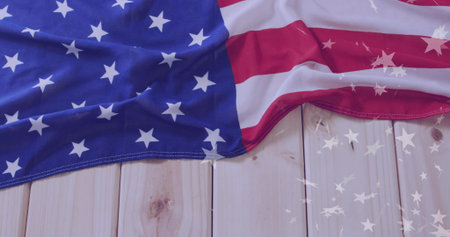 Displaying draped American flag on light wood planks, with star reflections across surface....