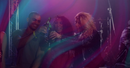 Raising trio of friends toasting at nightclub stage, with beer bottles, drum kit and stage lights....