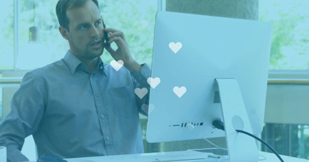 Talking worker wearing blue shirt holding smartphone looking at computer at office, copy space....